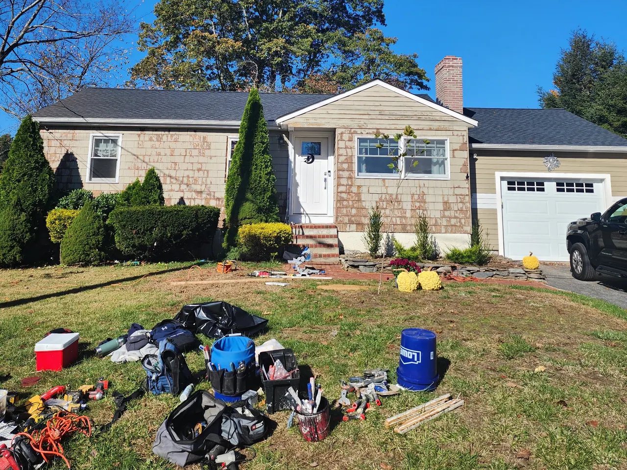 Before: ranch house with weathered tan cedar shingles, white garage door, painting gear on the lawn