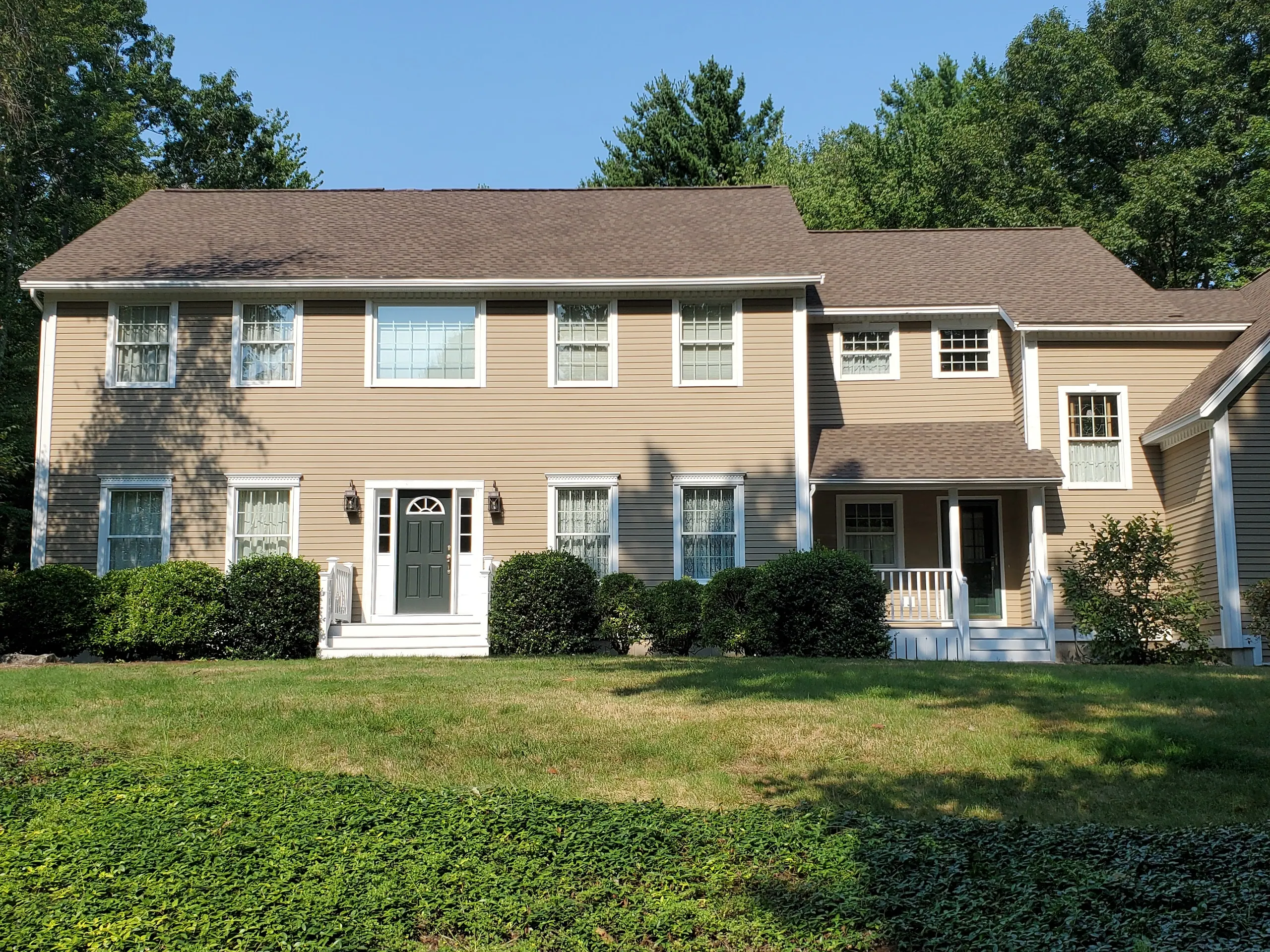 Two-story colonial with tan siding and white trim, freshly painted, above a fieldstone wall and lawn